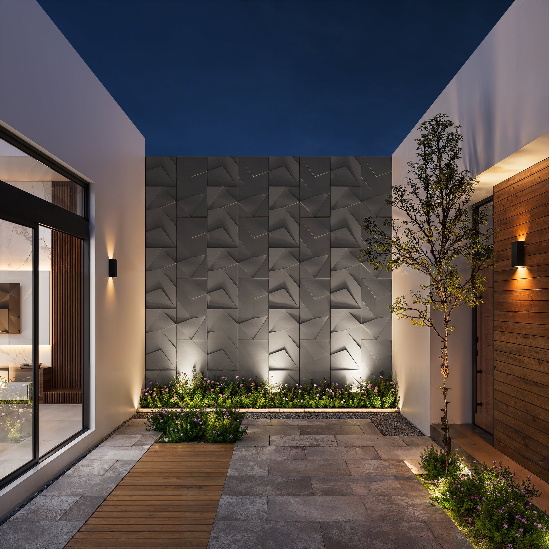 Modern outdoor patio with geometric wall, plants, and pathway at night.